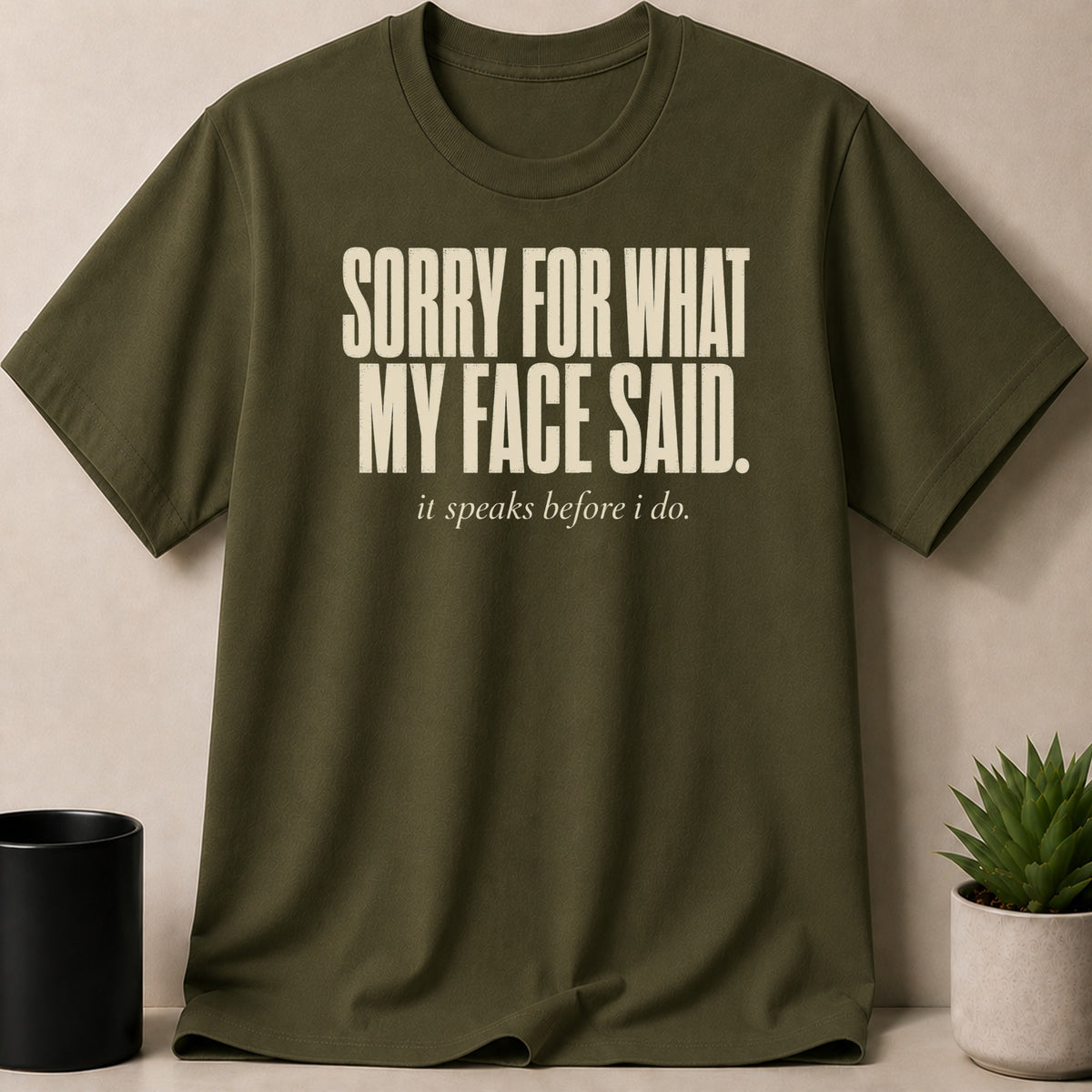 Olive green t-shirt with bold white text: "SORRY FOR WHAT MY FACE SAID," and smaller text below: "it speaks before i do."