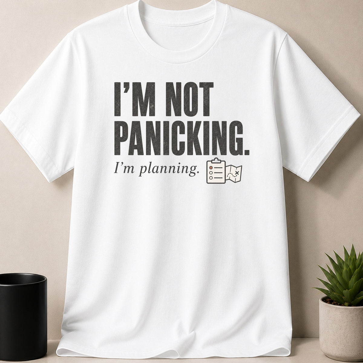 White t-shirt with "I'm NOT PANICKING. I'm planning." text and planning icons.