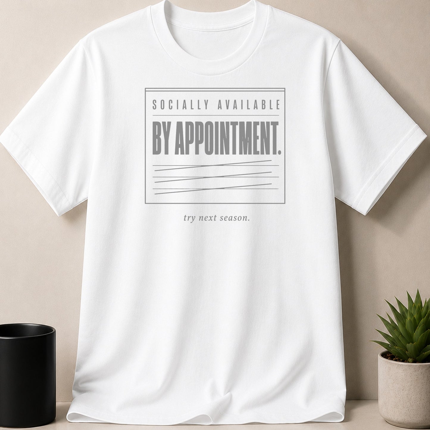 White t-shirt with gray text "SOCIALLY AVAILABLE BY APPOINTMENT. try next season."