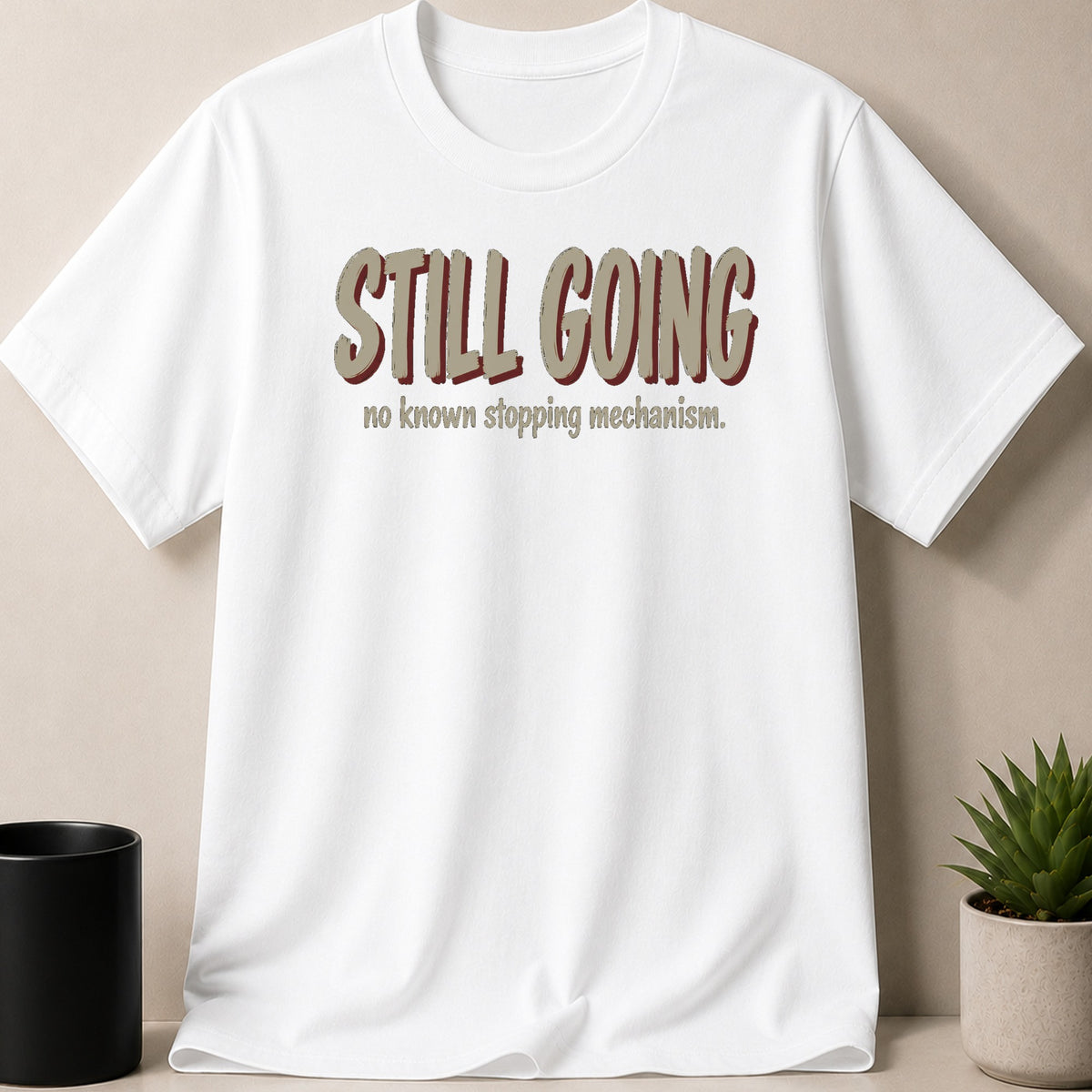 White t-shirt with "STILL GOING no known stopping mechanism." text.