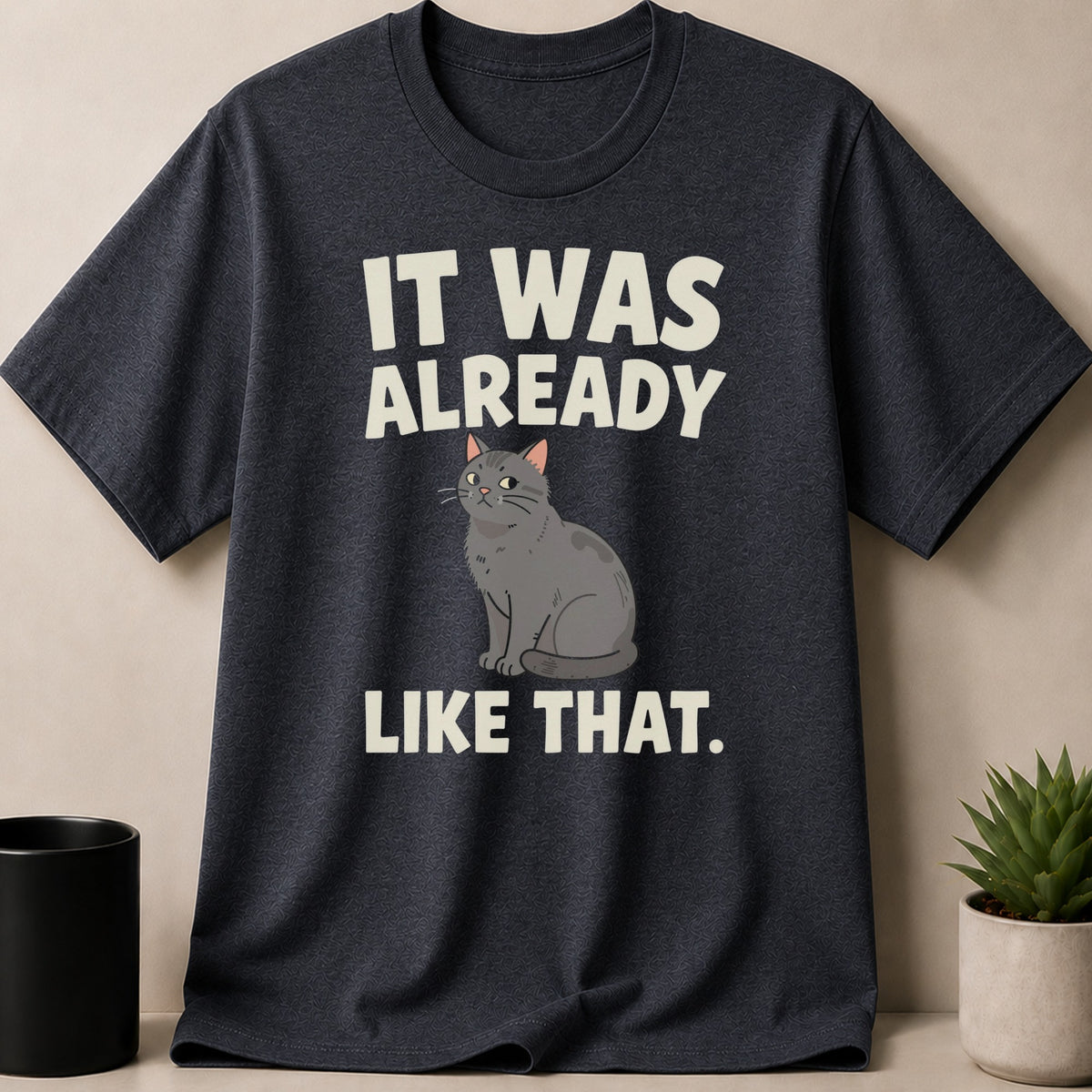 A dark grey t-shirt featuring a cartoon grey cat illustration and white text reading IT WAS ALREADY LIKE THAT.