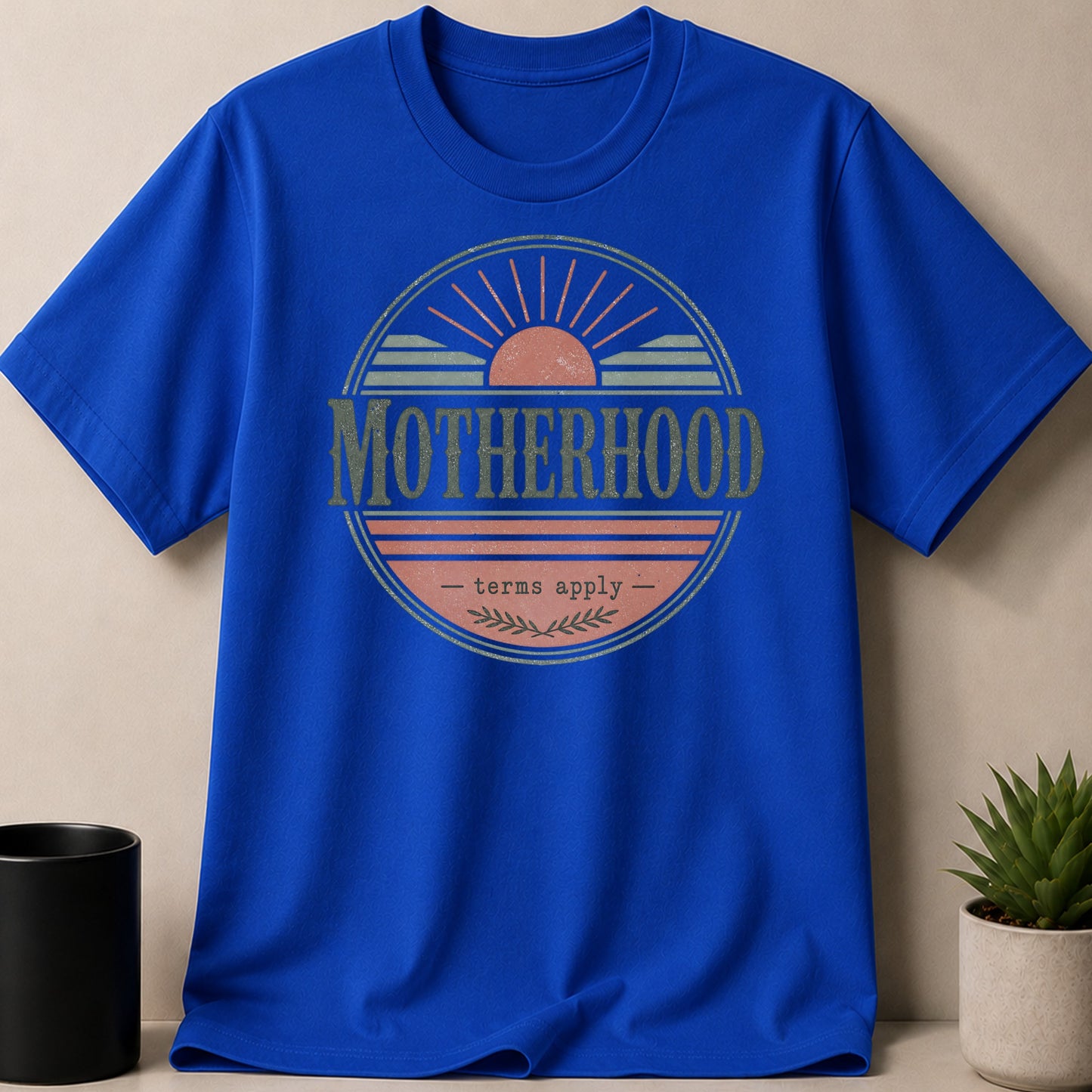 Blue t-shirt with "Motherhood - terms apply -" sun graphic.