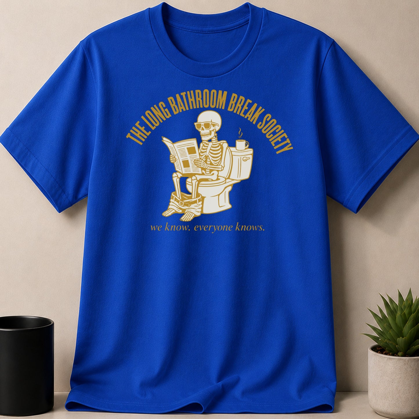 Blue t-shirt with a skeleton on a toilet reading a newspaper.