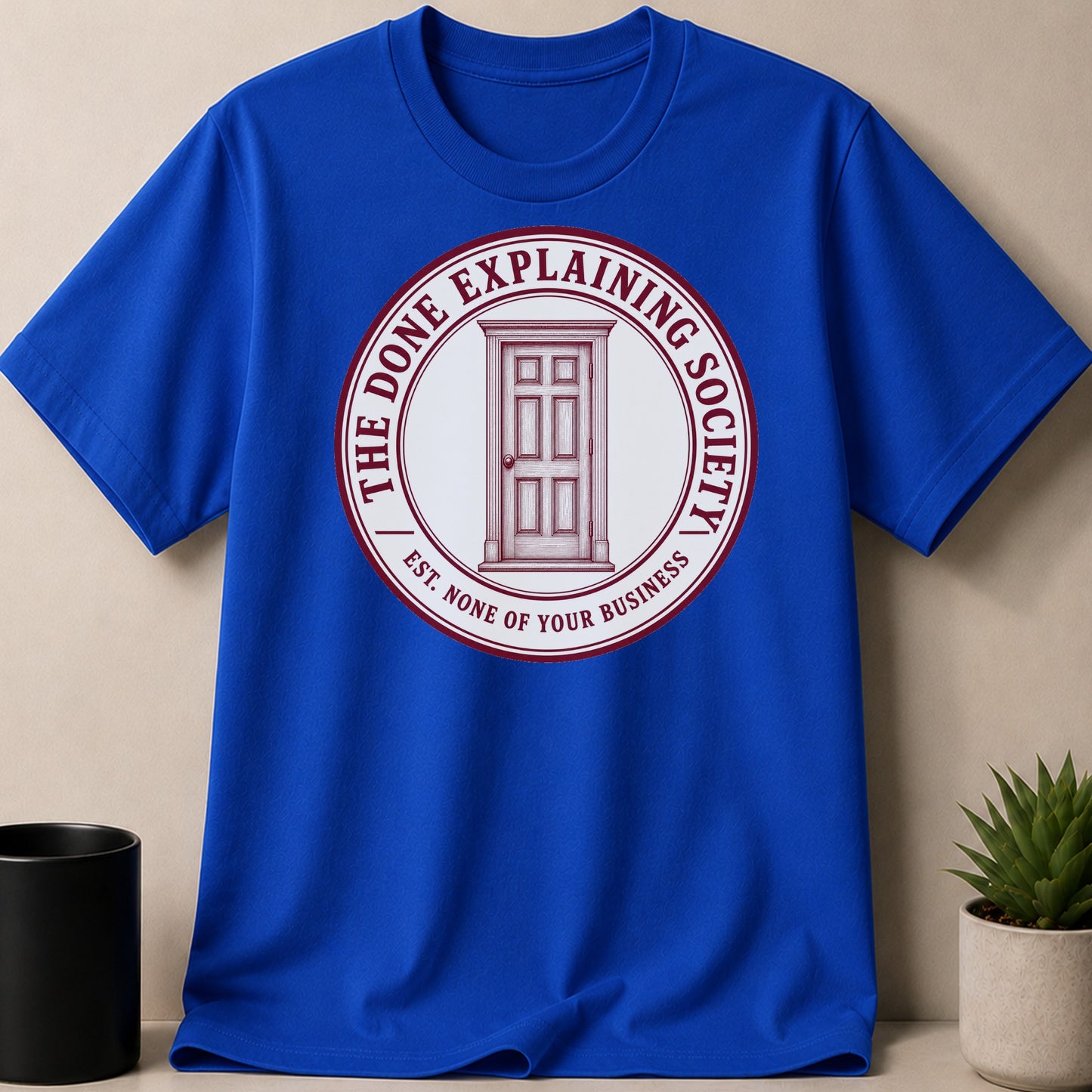 Blue t-shirt with circular logo of a door and text "The Done Explaining Society".