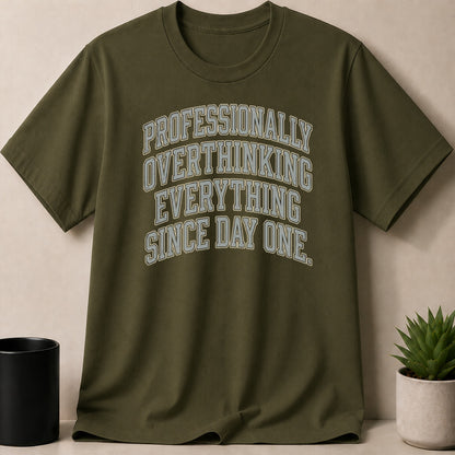 Olive green t-shirt with the text "PROFESSIONALLY OVERTHINKING EVERYTHING SINCE DAY ONE."