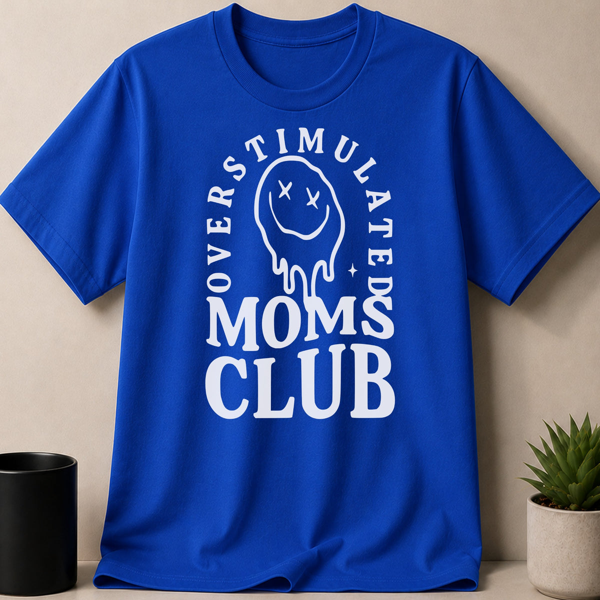 Royal blue t-shirt with white text reading "OVERSTIMULATED MOMS CLUB" and a dripping smiley face.