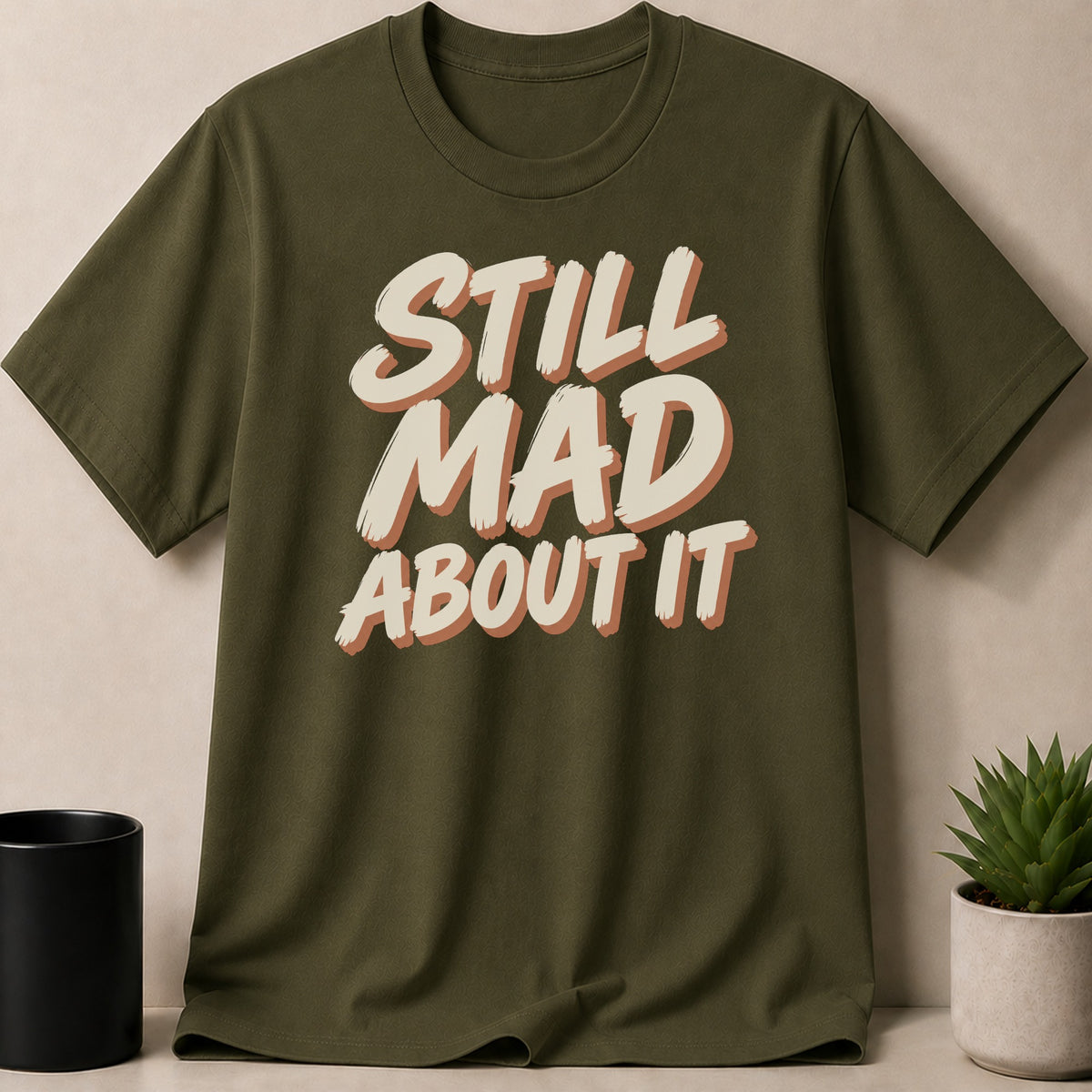 Olive green t-shirt with "STILL MAD ABOUT IT" text graphic.