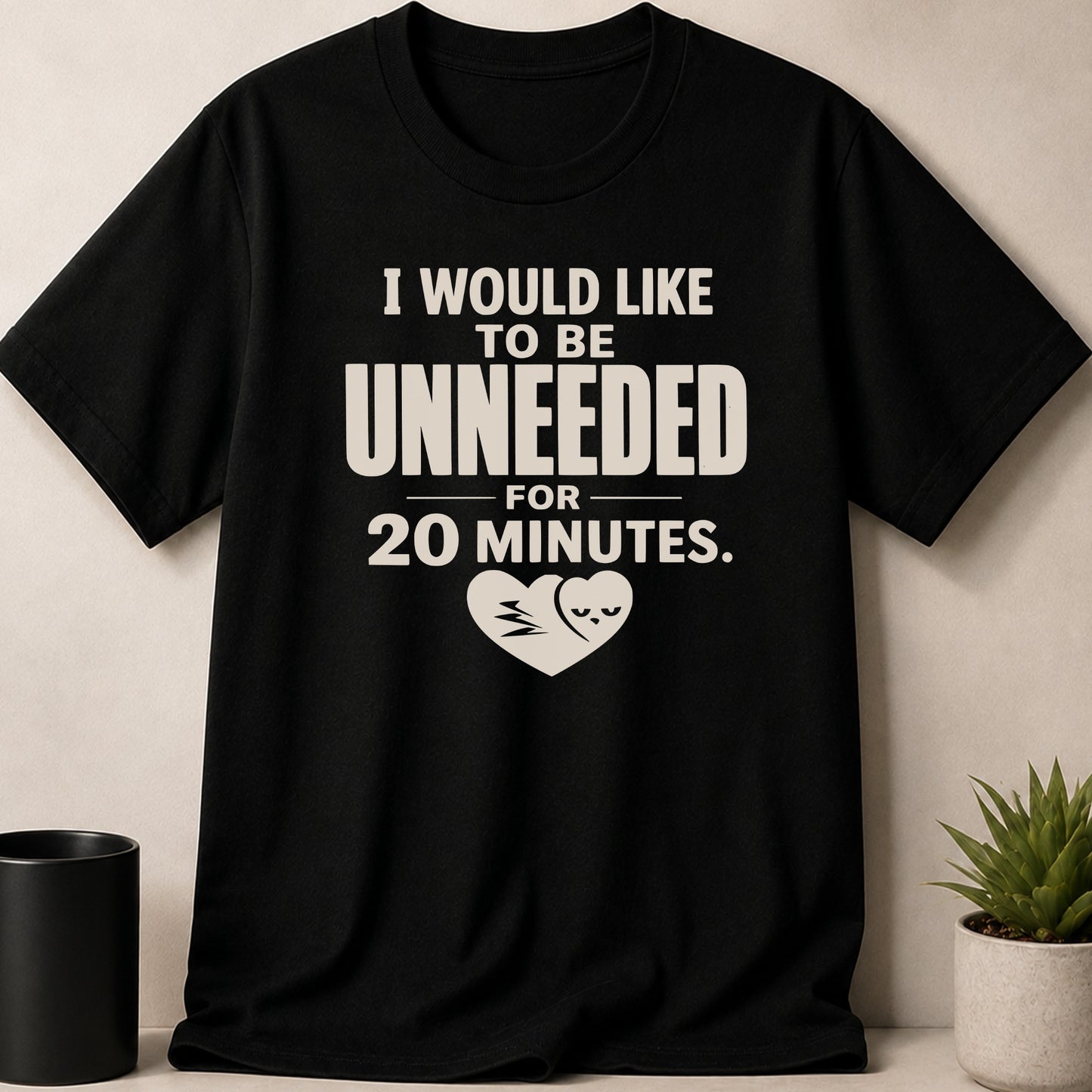 Black t-shirt with "I would like to be unneeded for 20 minutes." and a heart with a grumpy face.