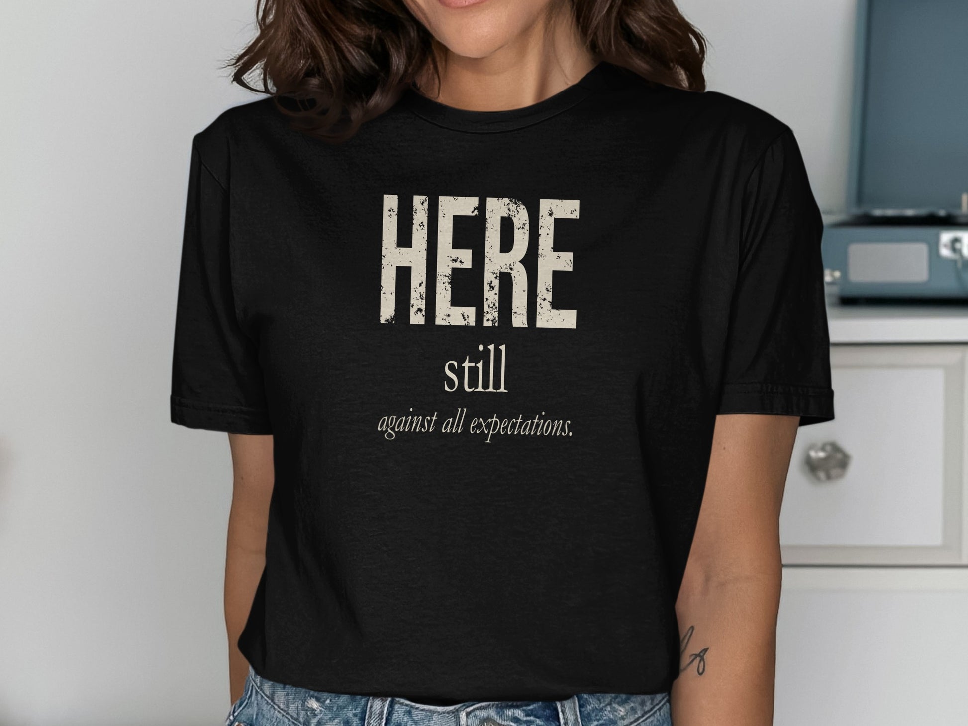 Black t-shirt with text "HERE still against all expectations."