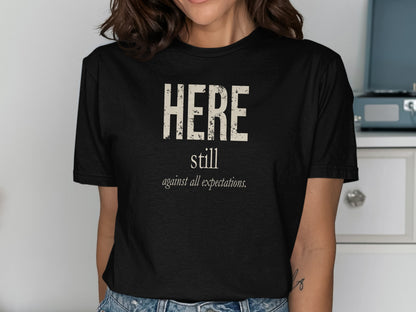 Black t-shirt with text "HERE still against all expectations."
