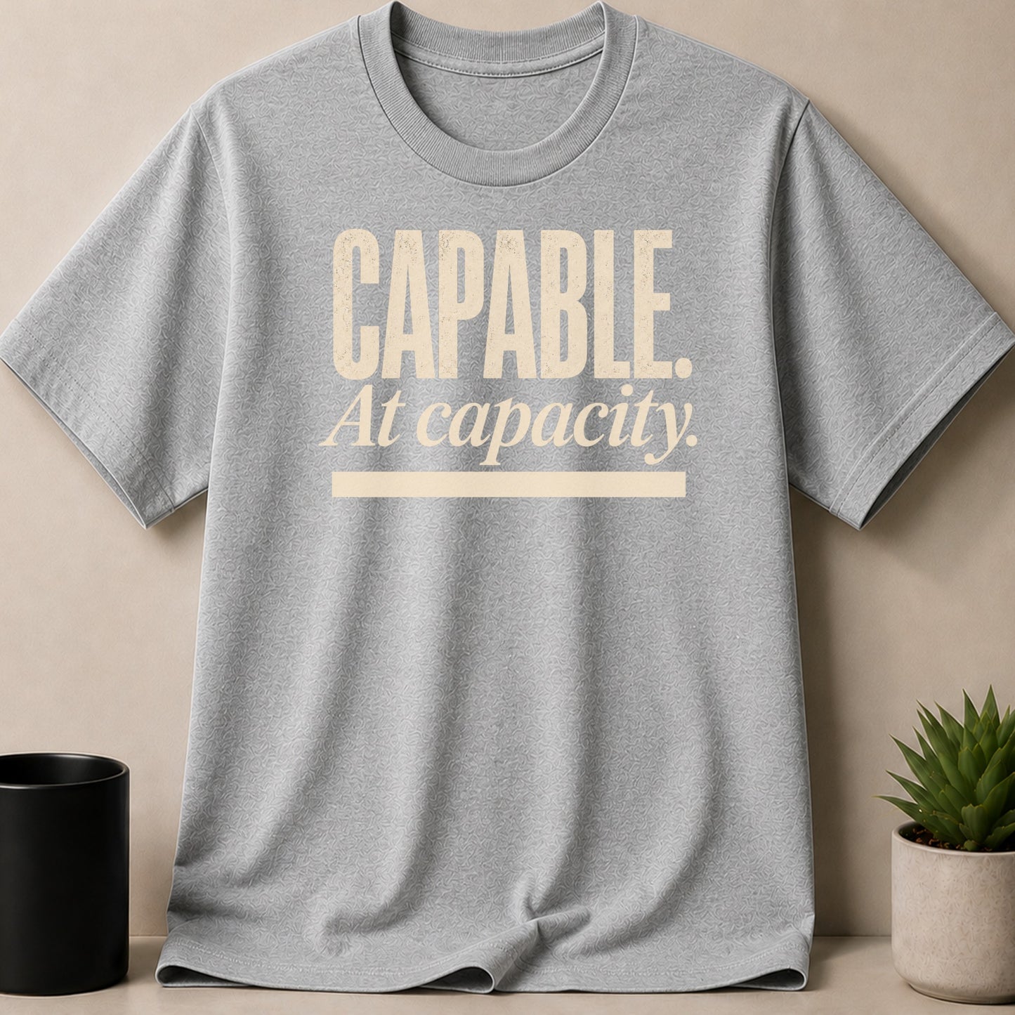 Grey t-shirt with cream text reading "CAPABLE. At capacity."