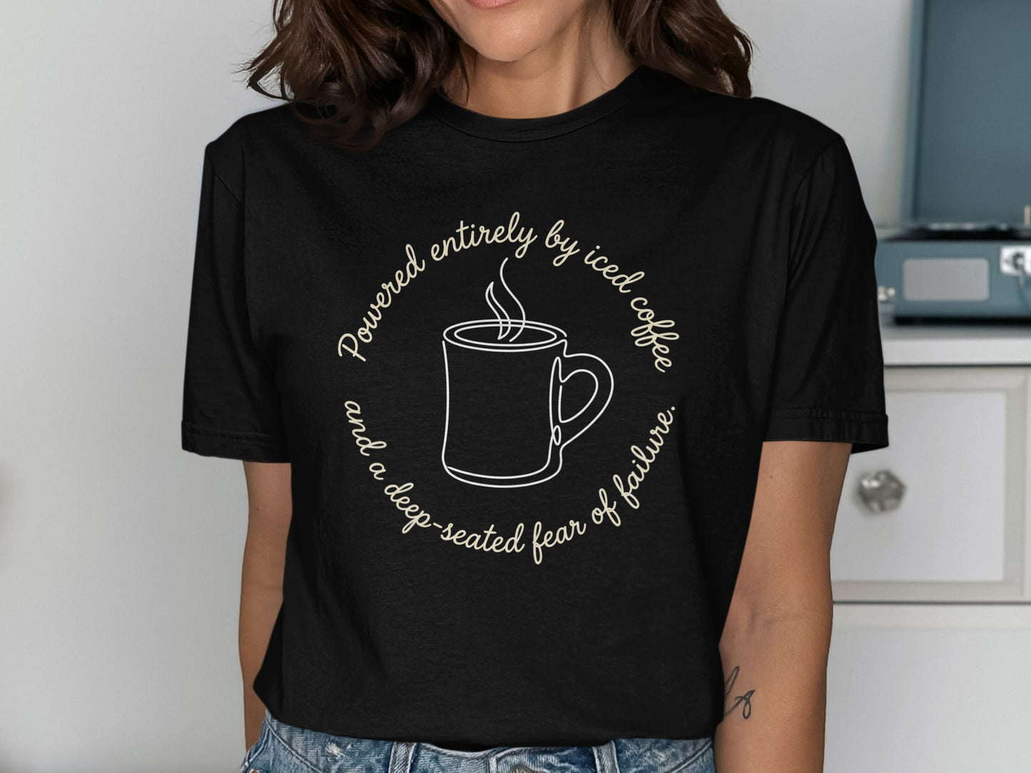 Black t-shirt with text: Powered entirely by iced coffee and a deep-seated fear of failure.