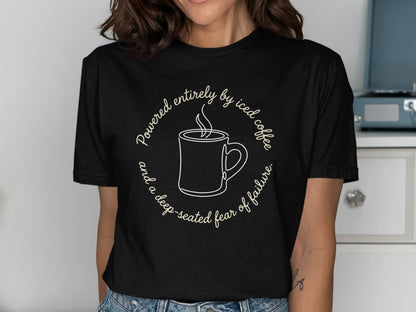 Black t-shirt with text: Powered entirely by iced coffee and a deep-seated fear of failure.