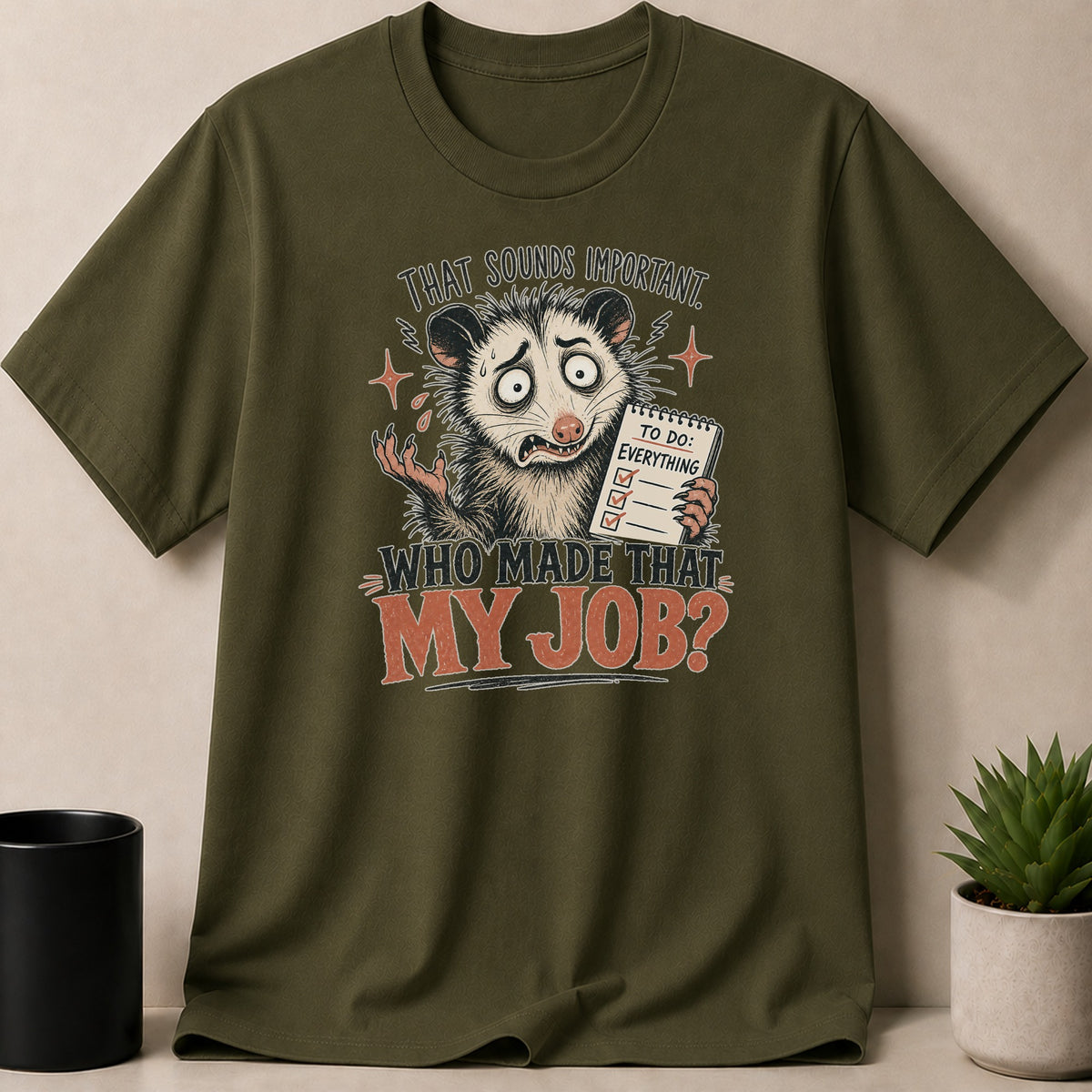 Green t-shirt with opossum graphic saying "That sounds important. Who made that my job?"