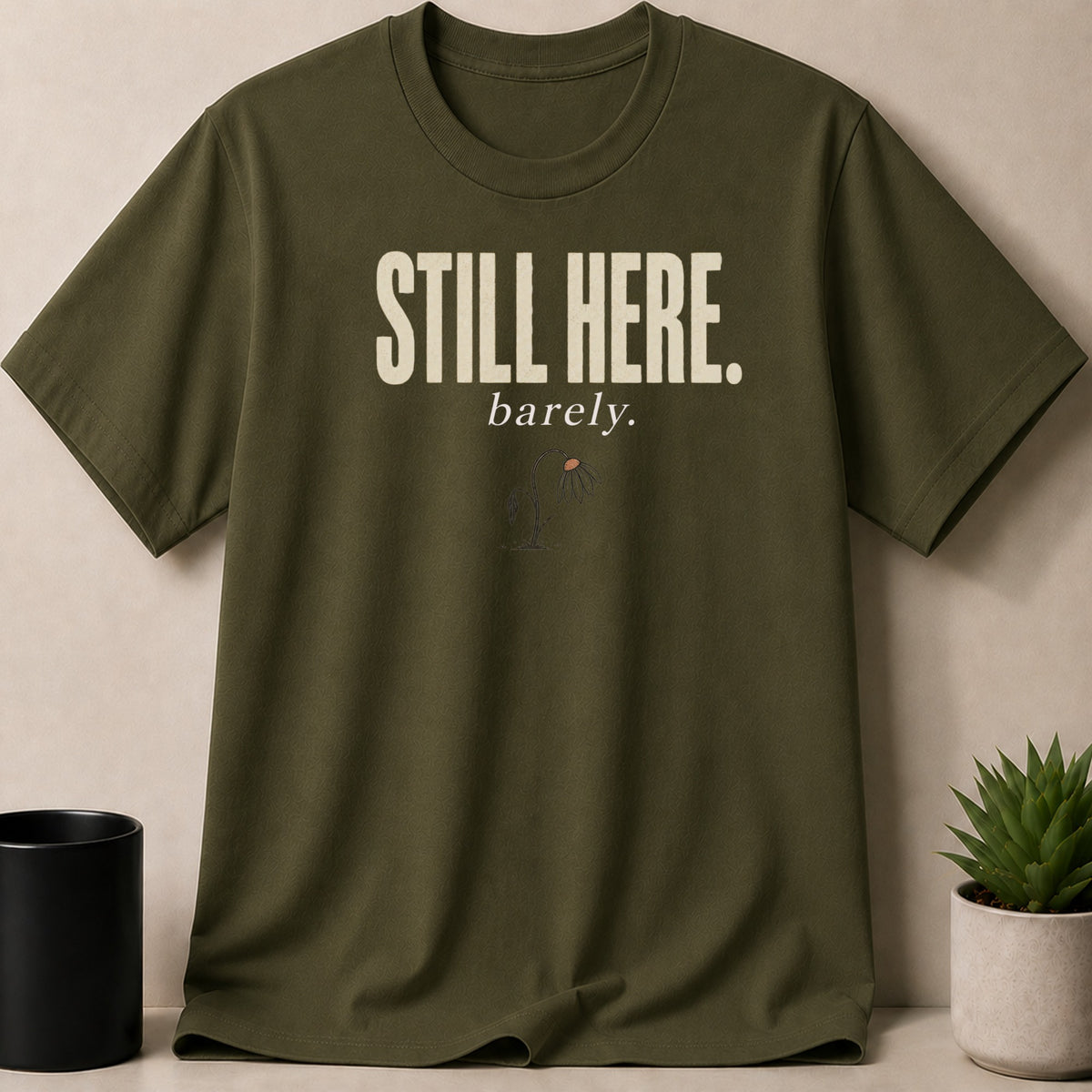 Olive green t-shirt with "STILL HERE." and a wilting flower graphic.