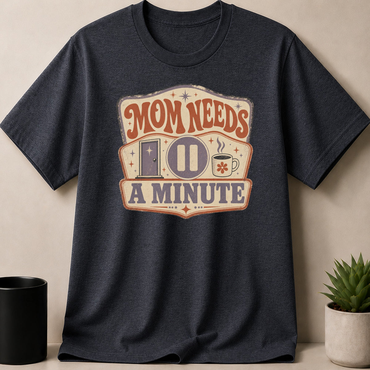 Dark gray t-shirt with "Mom Needs A Minute" text and graphic.