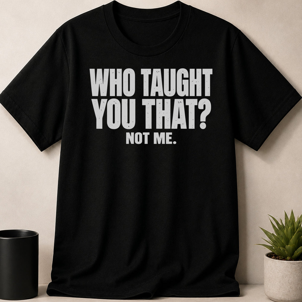 A black short-sleeved t-shirt with white distressed text that reads WHO TAUGHT YOU THAT? NOT ME.