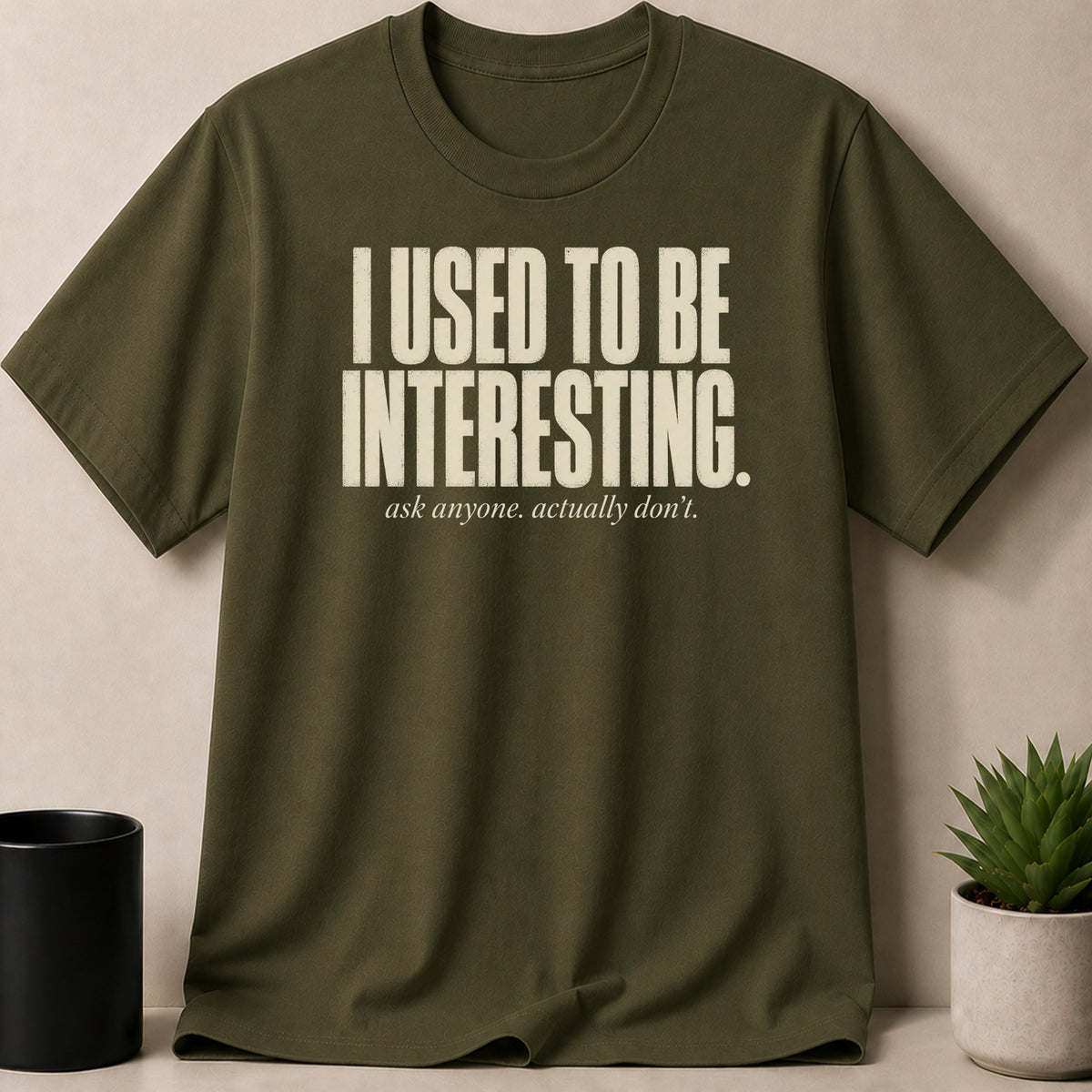 Olive green t-shirt with white text "I USED TO BE INTERESTING. ask anyone. actually don't."