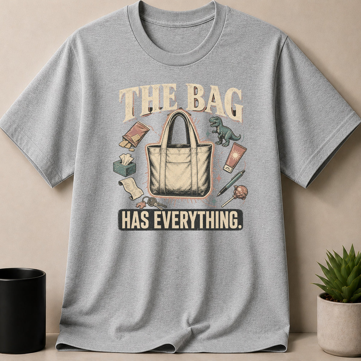 Gray t-shirt with a graphic of a tote bag surrounded by various items and text.
