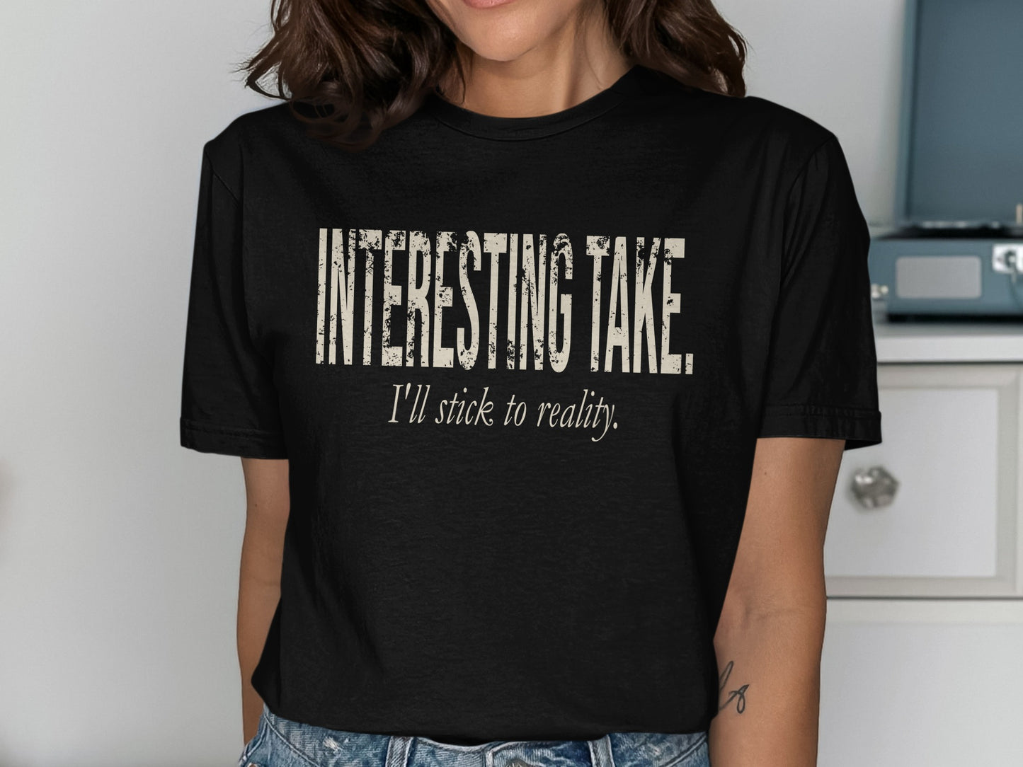 Black t-shirt with "INTERESTING TAKE. I'll stick to reality." slogan.