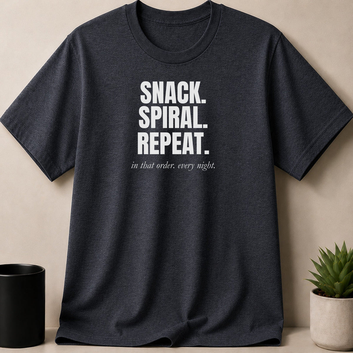 Dark gray t-shirt with white text "SNACK. SPIRAL. REPEAT." and "in that order. every night."