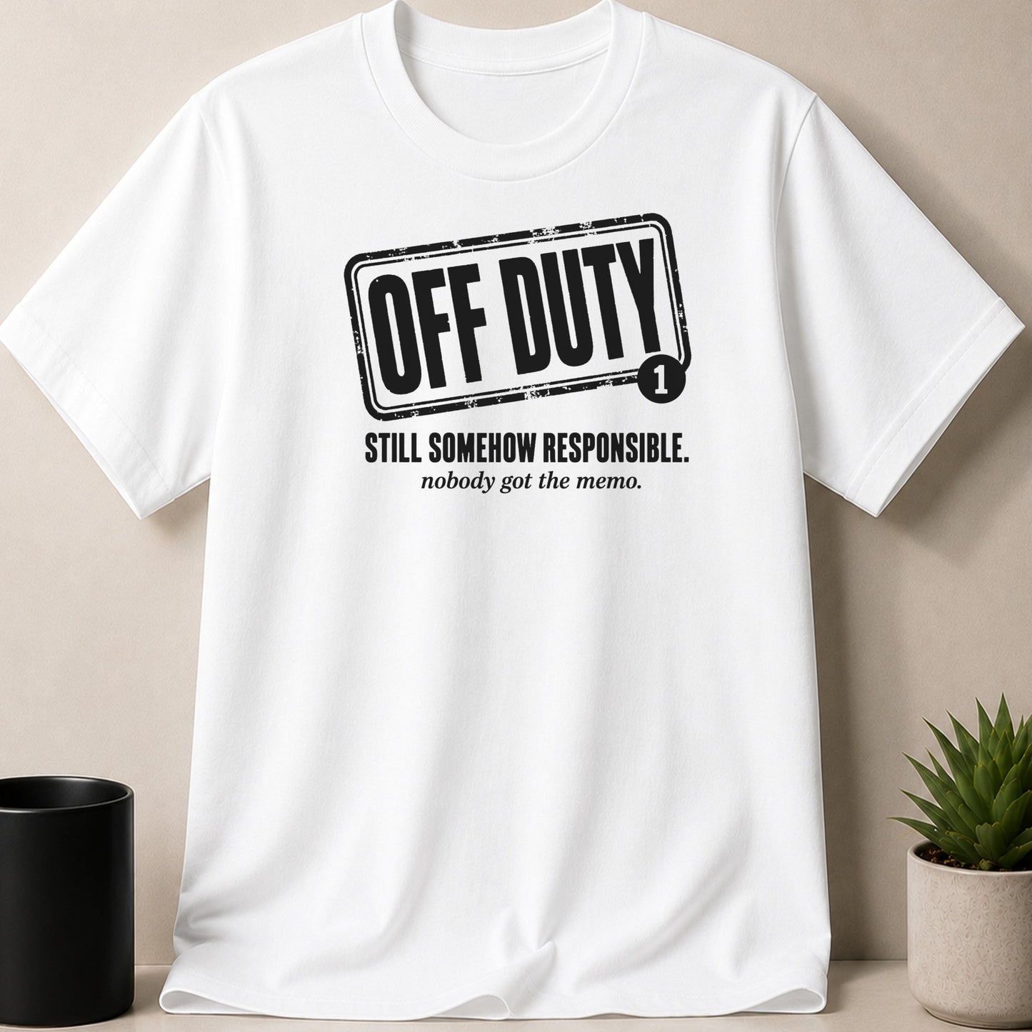 White t-shirt with black graphic: "OFF DUTY" and "STILL SOMEHOW RESPONSIBLE. nobody got the memo."