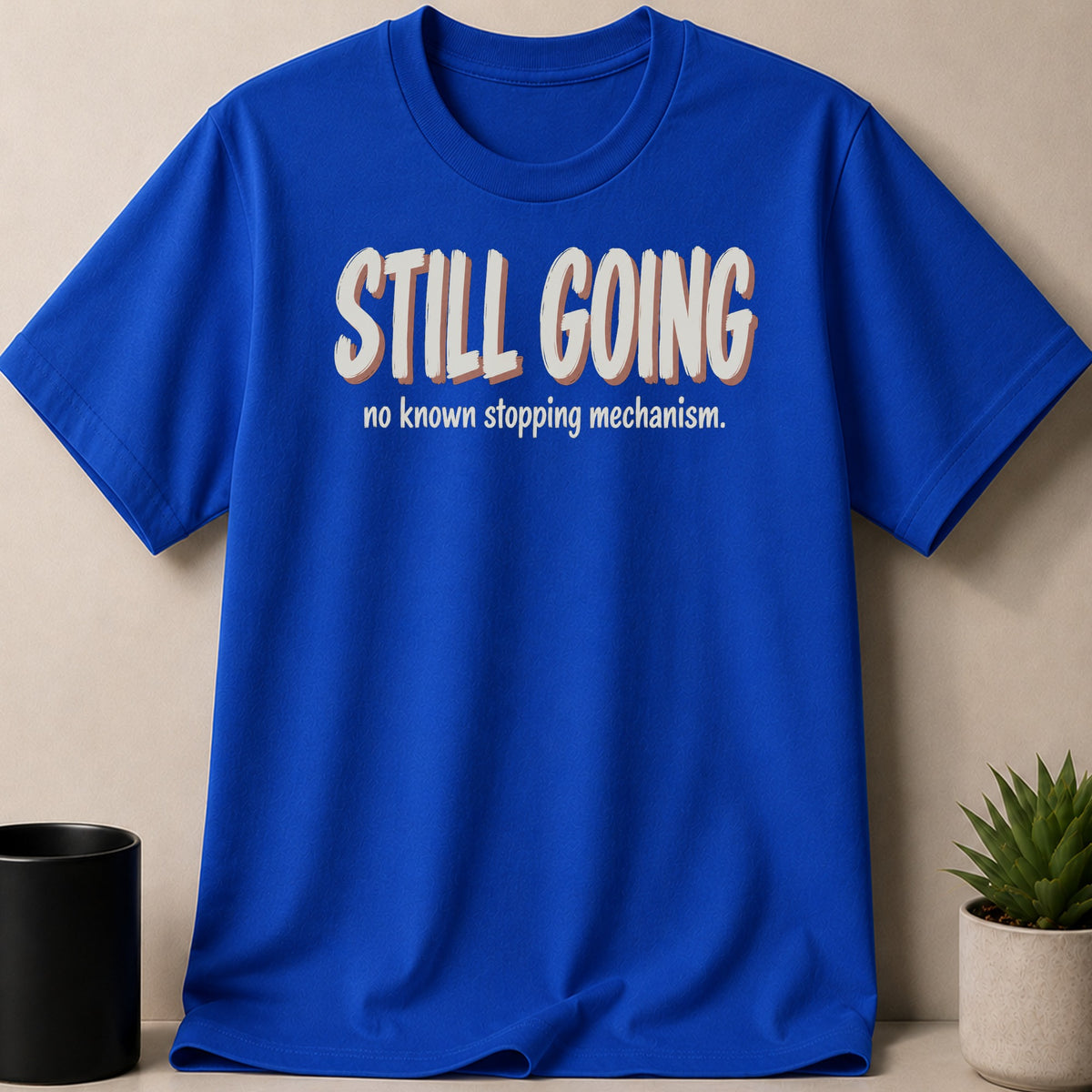 Royal blue t-shirt with "STILL GOING" and "no known stopping mechanism." text.