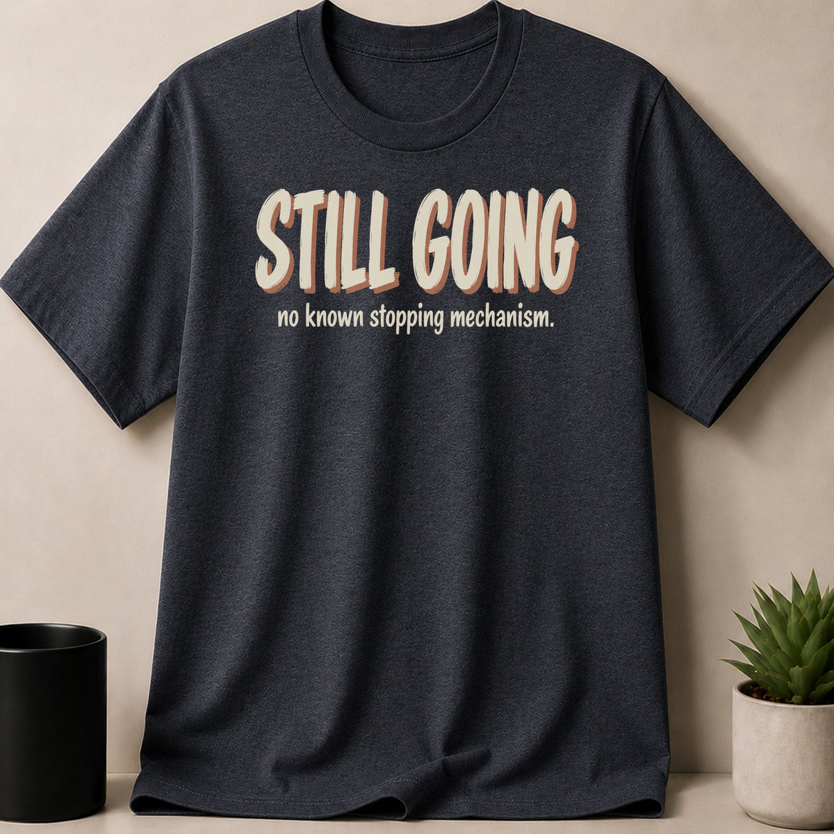 Dark gray t-shirt with "STILL GOING no known stopping mechanism." text.