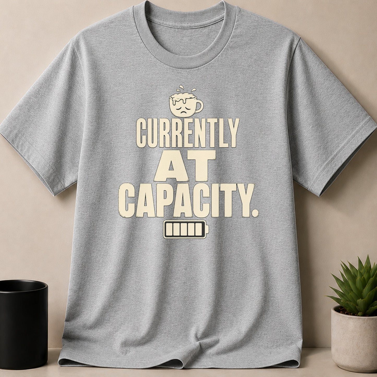 Gray t-shirt with "CURRENTLY AT CAPACITY" text and a sad coffee cup graphic.