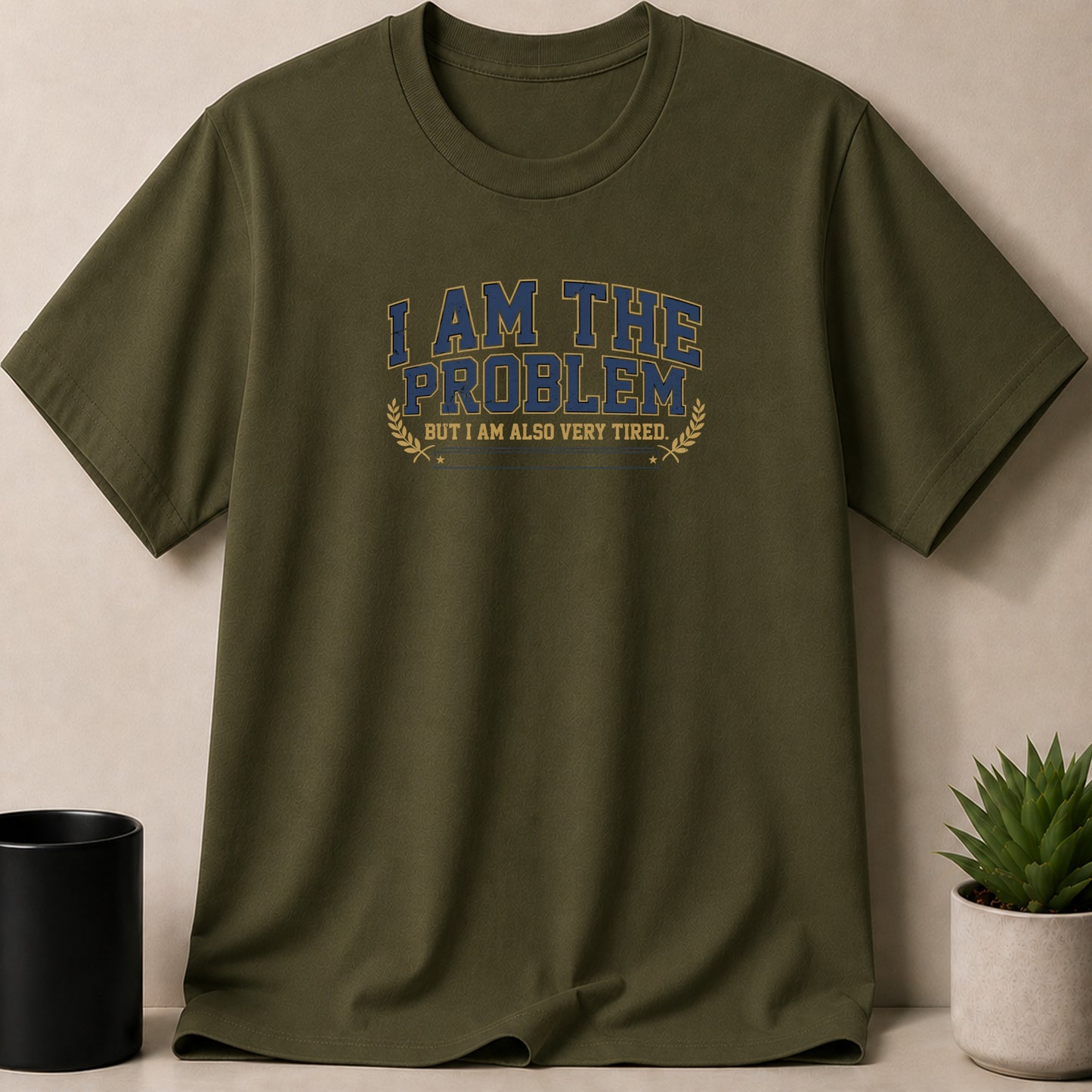 Olive green t-shirt with blue and yellow text: "I AM THE PROBLEM BUT I AM ALSO VERY TIRED."