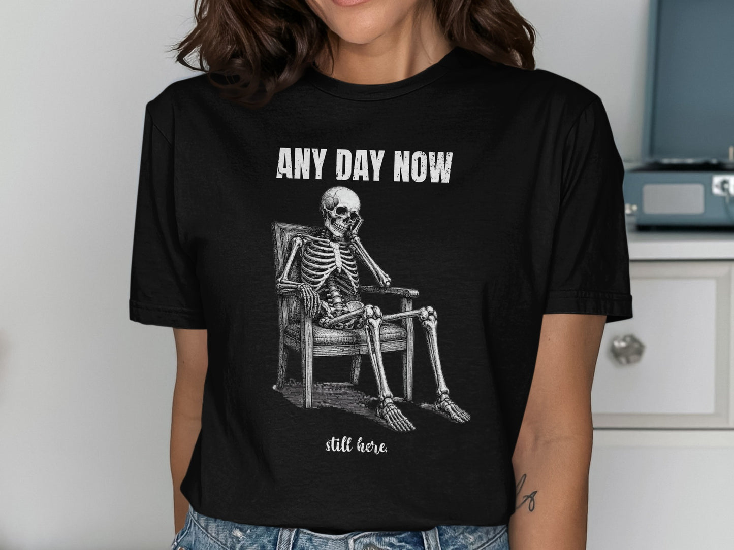 Skeleton sitting in chair with text "ANY DAY NOW" and "still here."