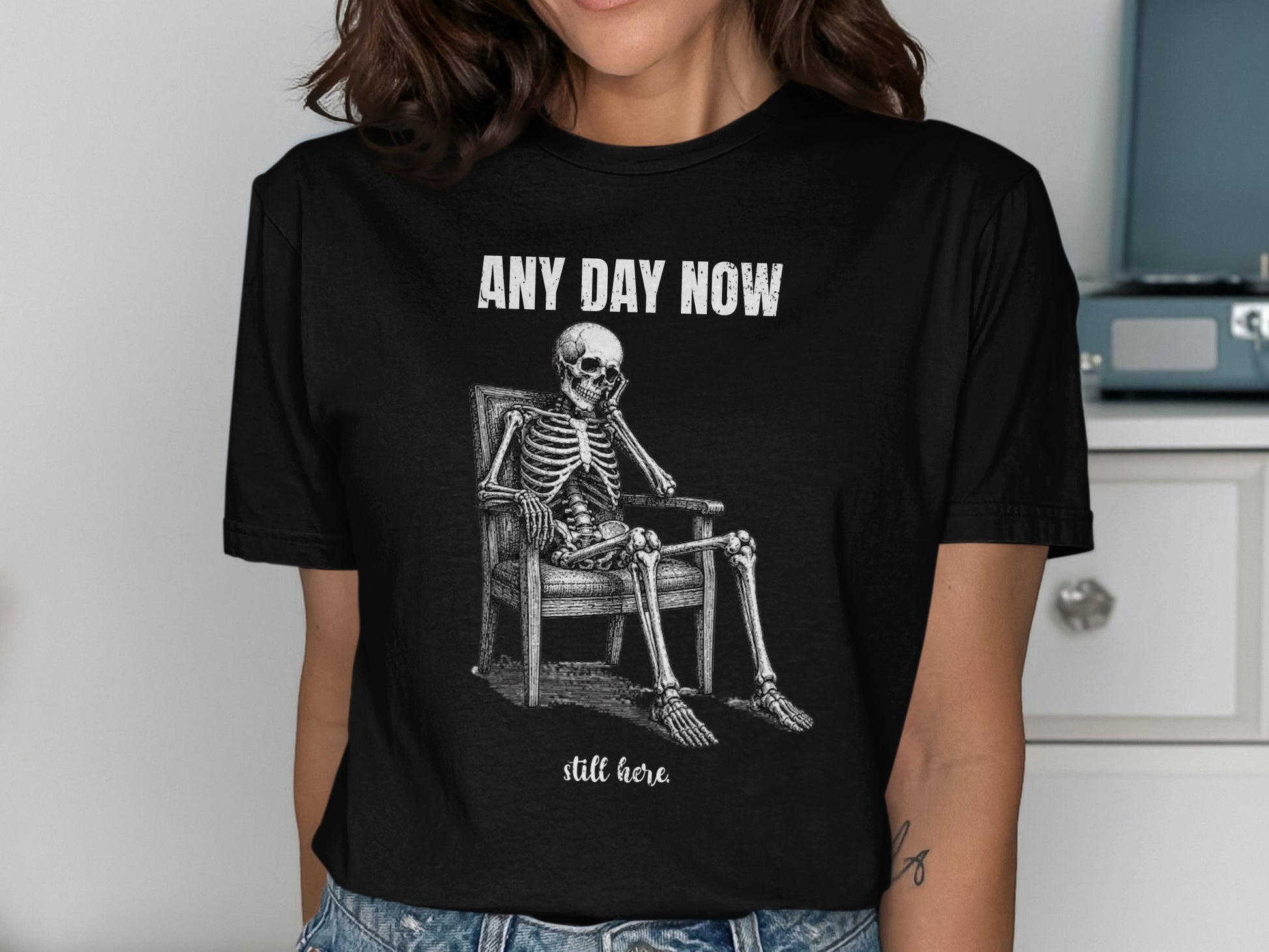 Skeleton sitting in chair with text "ANY DAY NOW" and "still here."