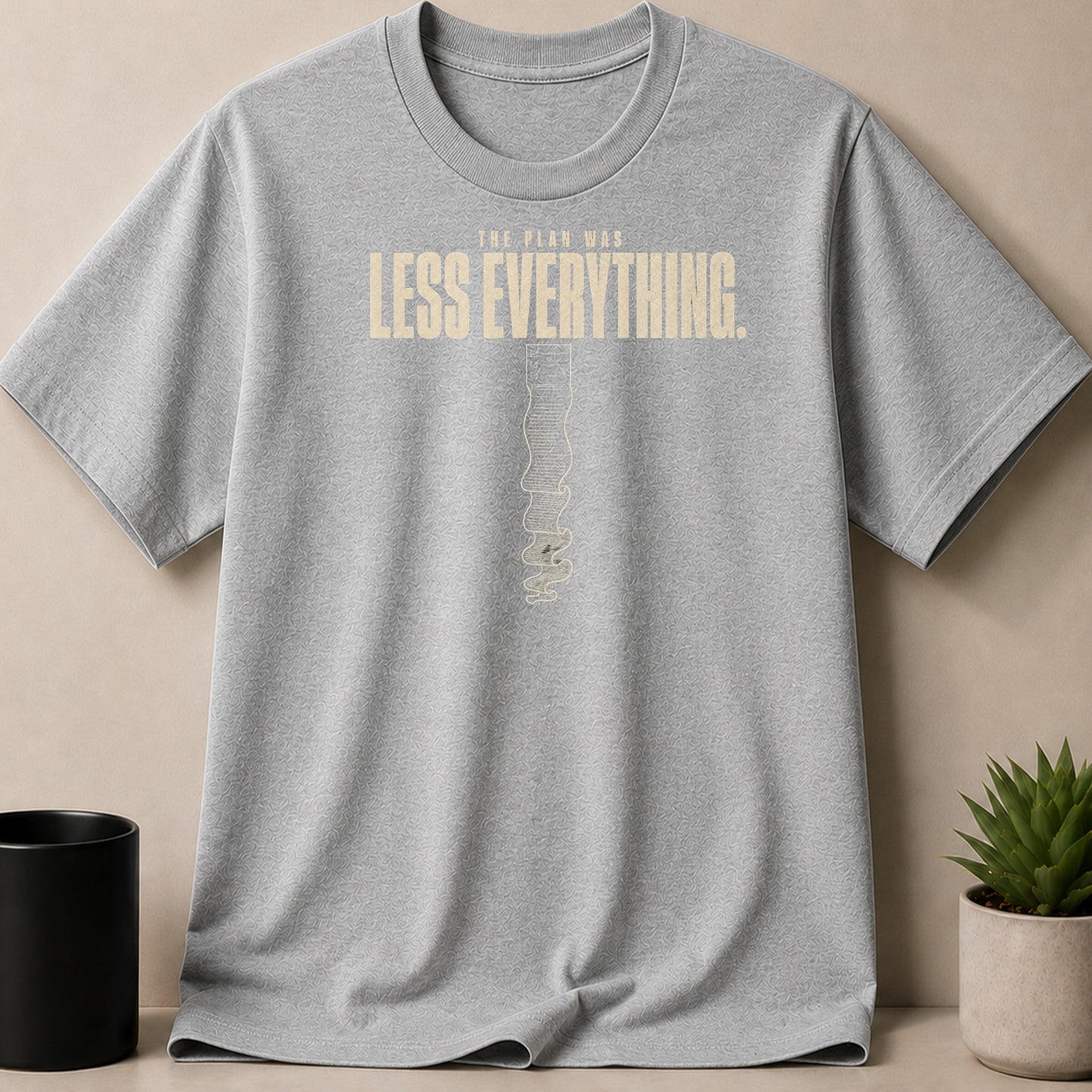 Grey t-shirt with "THE PLAN WAS LESS EVERYTHING." text and abstract design.