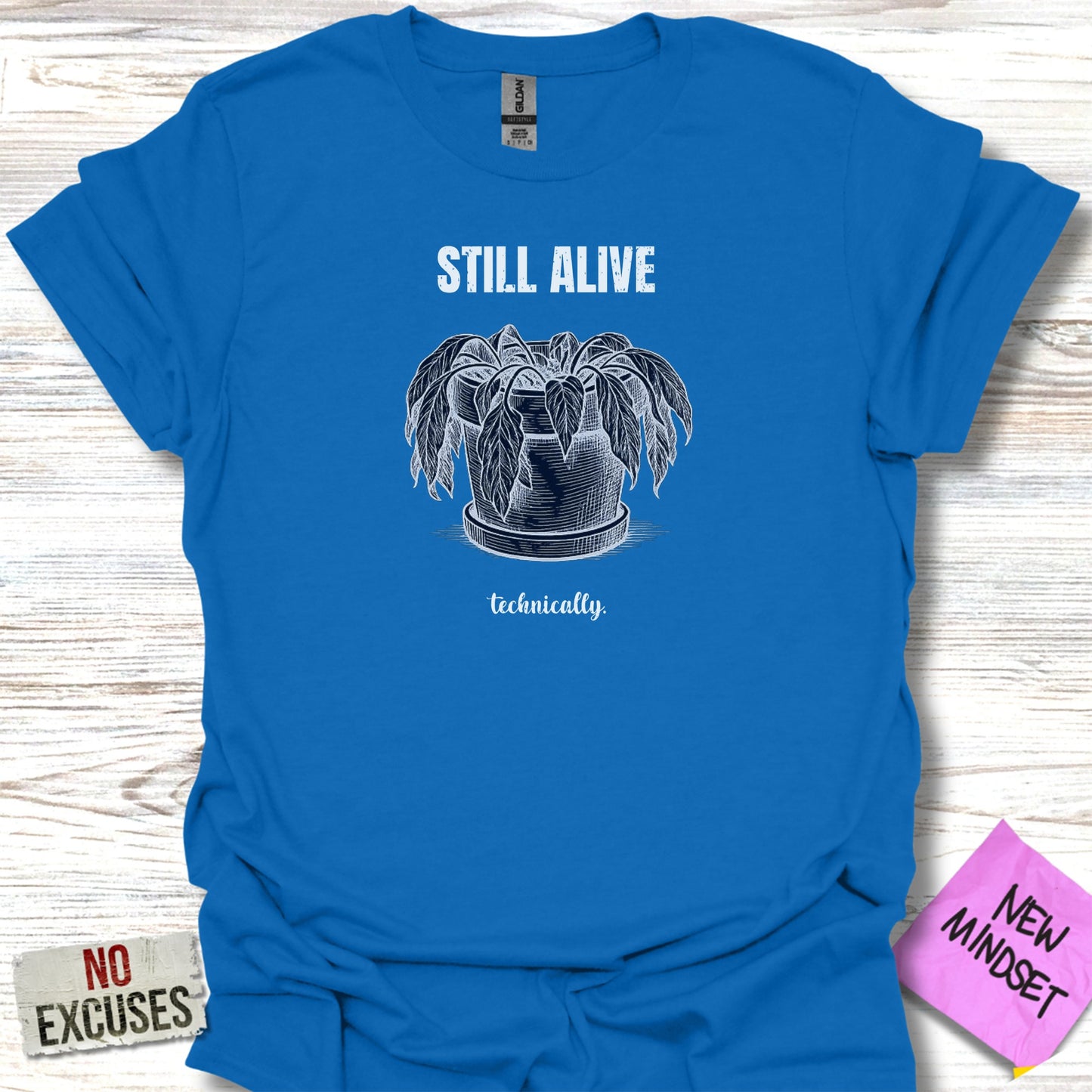 Blue t-shirt with an illustration of a potted plant and the text "STILL ALIVE technically."