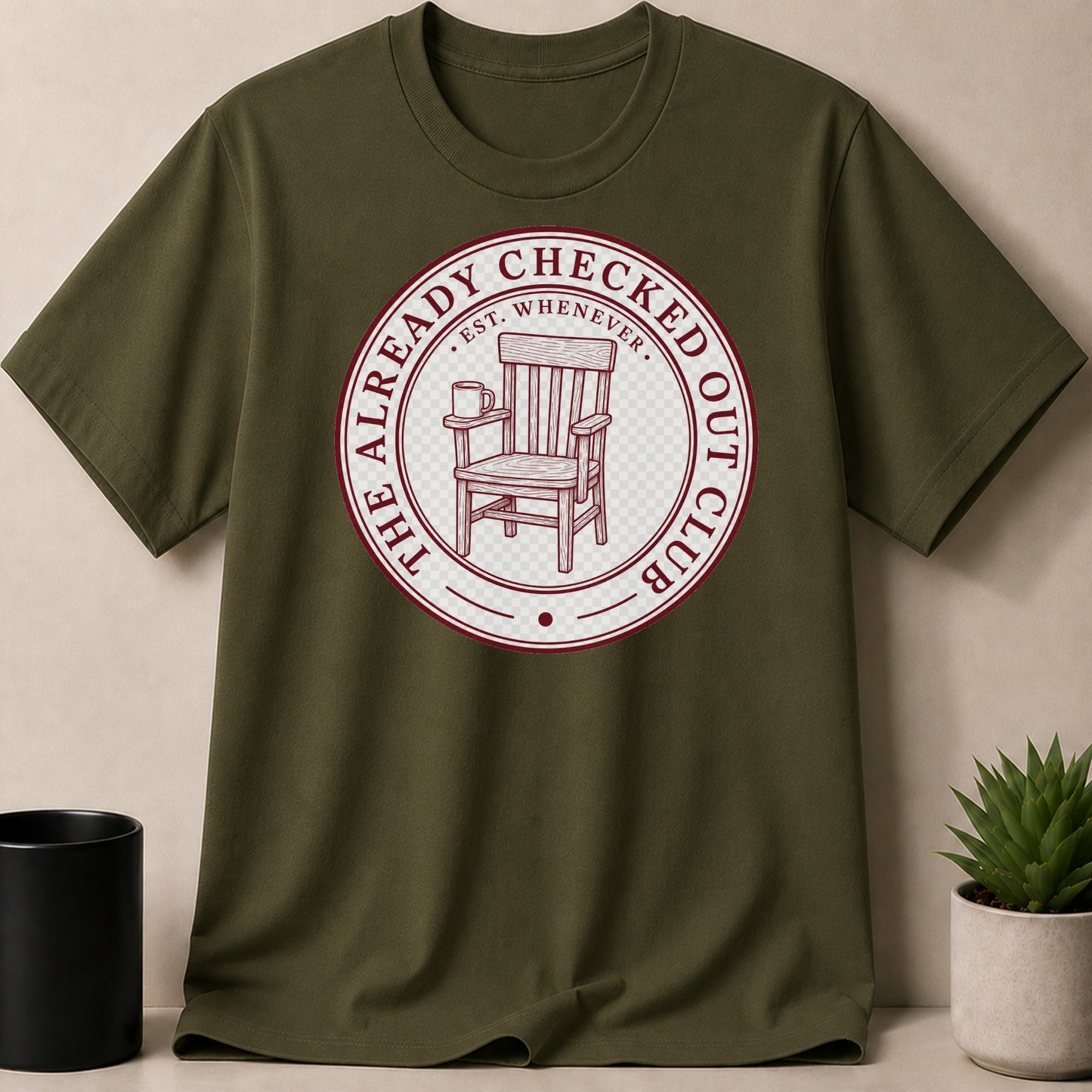 Green t-shirt with "The Already Checked Out Club" text, armchair, and mug graphic.