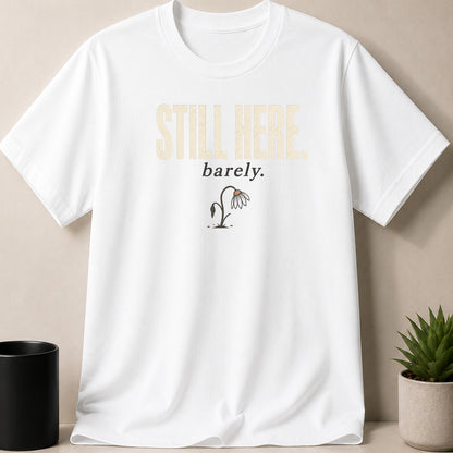 White t-shirt with "STILL HERE barely." text and wilted flower graphic.