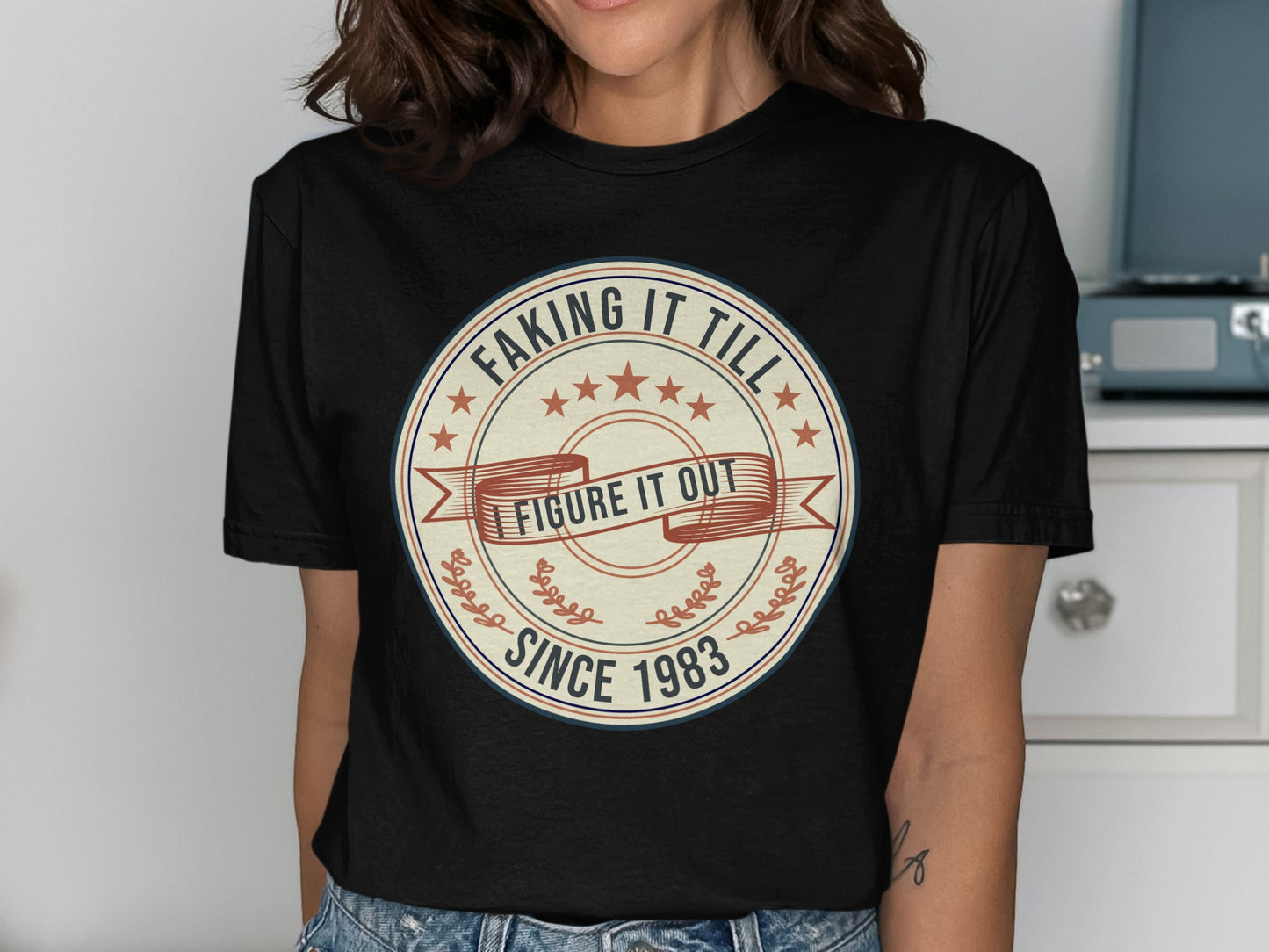 Black t-shirt with "Faking It Till I Figure It Out Since 1983" circular graphic.