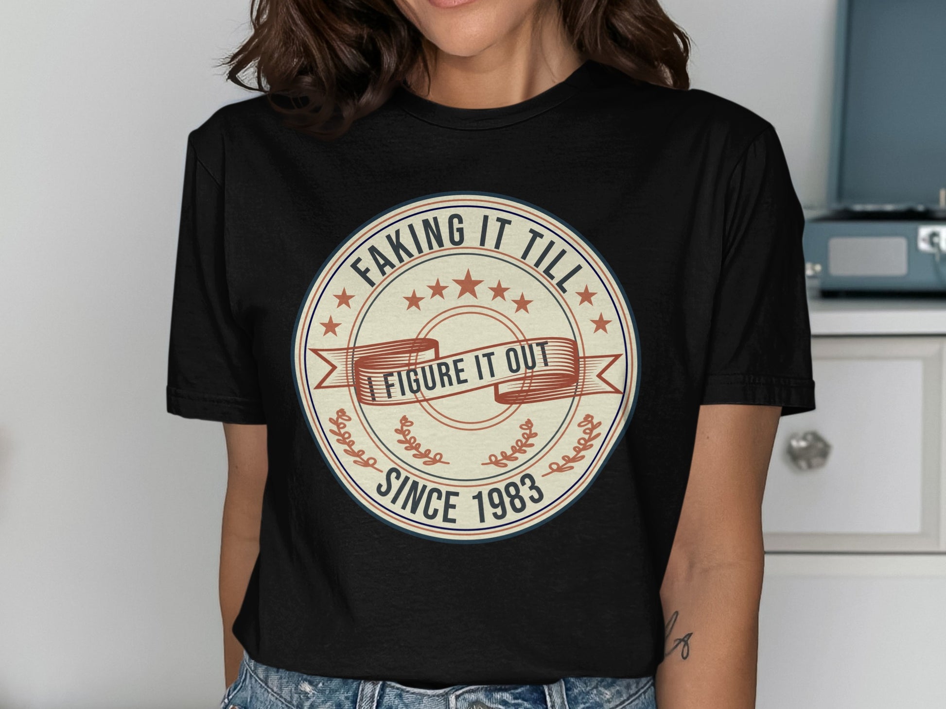 Black t-shirt with "Faking It Till I Figure It Out Since 1983" circular graphic.