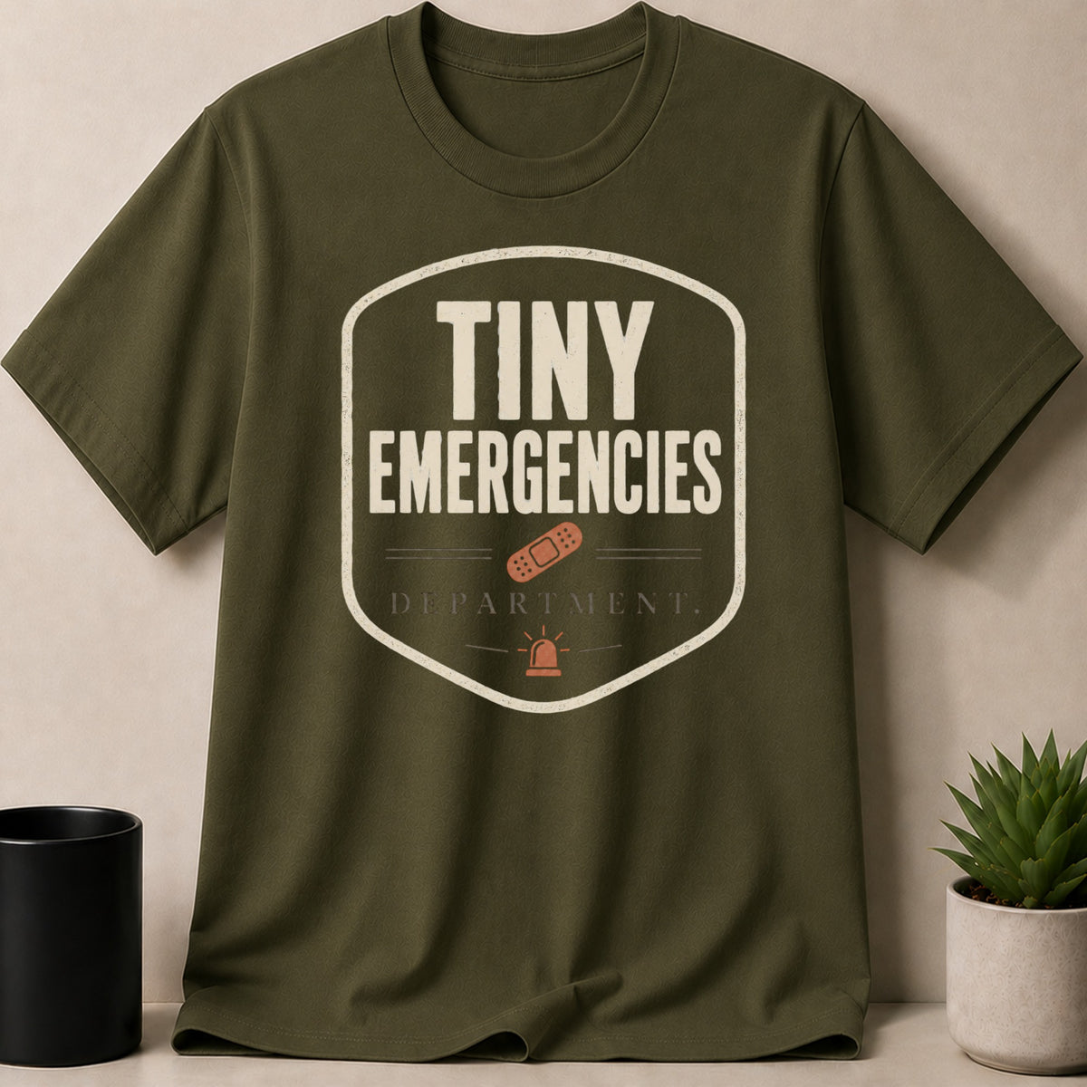 Olive green t-shirt with "Tiny Emergencies Department" text and graphics.