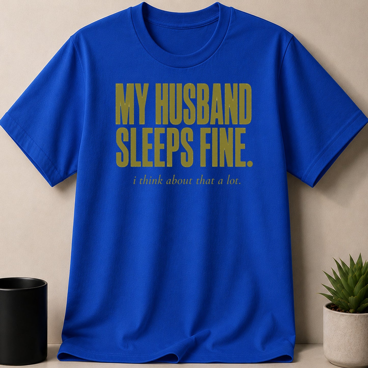 Blue t-shirt with gold text: "MY HUSBAND SLEEPS FINE. i think about that a lot."
