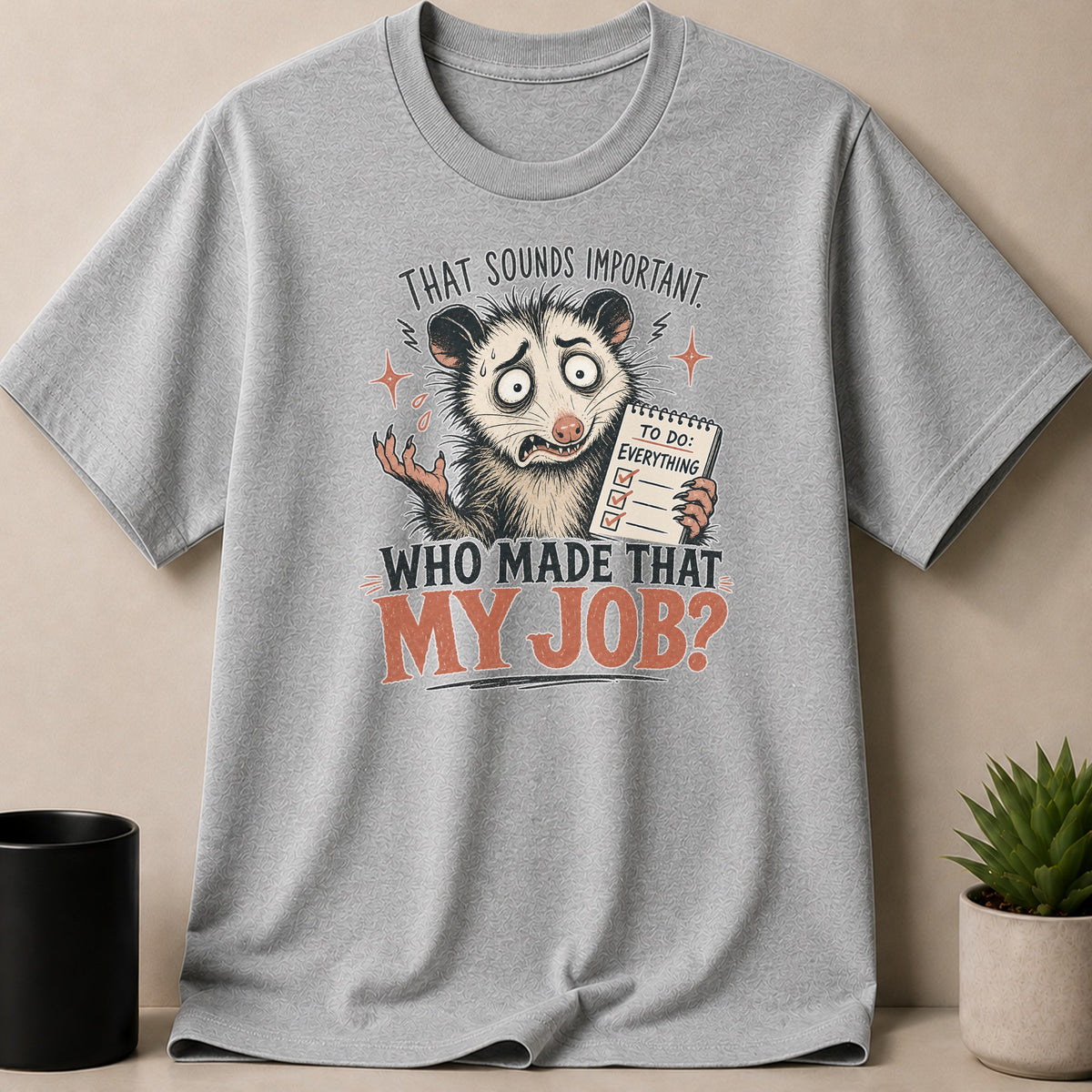 Grey t-shirt with opossum holding a "TO DO: EVERYTHING" notepad and text "WHO MADE THAT MY JOB?".