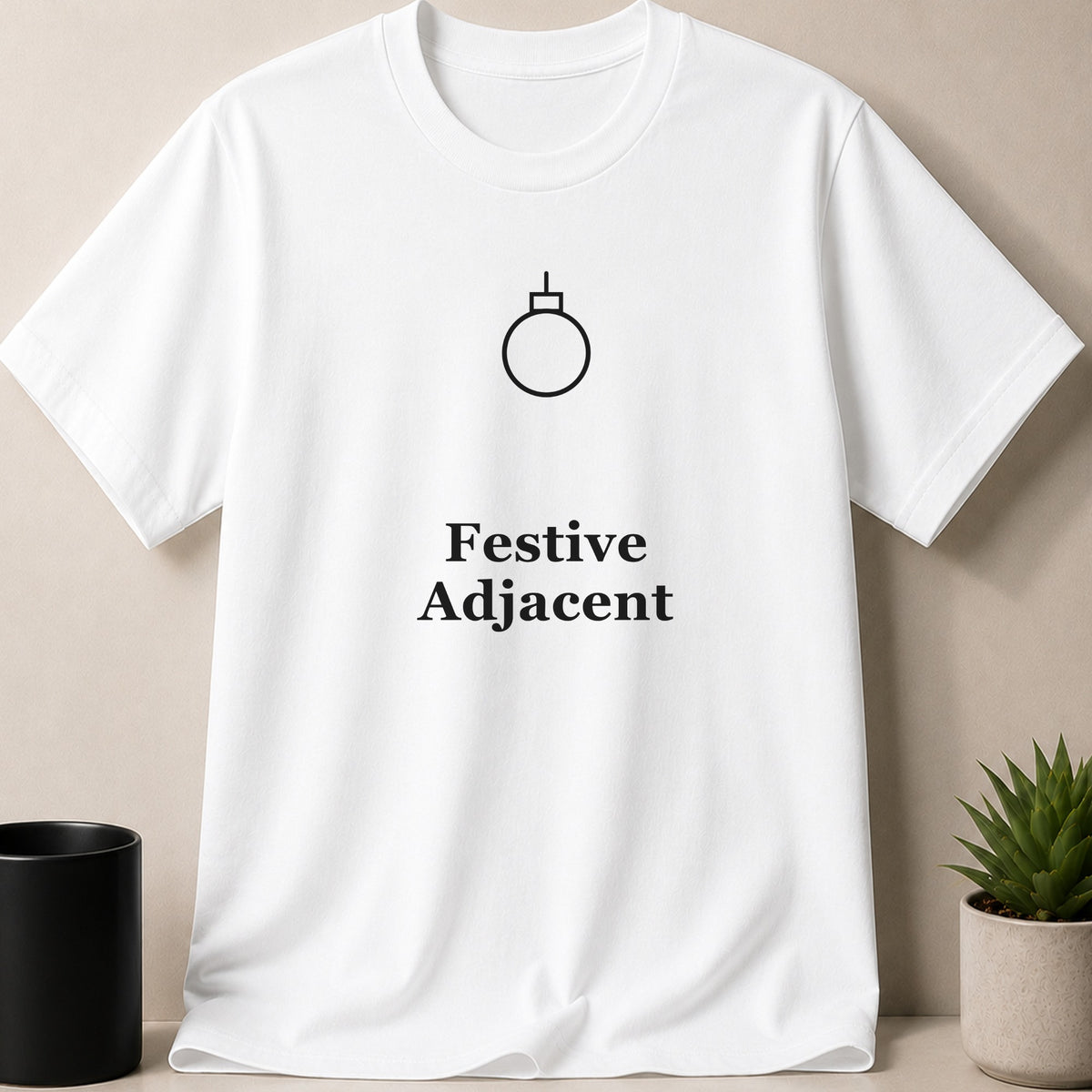 White short-sleeve t-shirt with a minimalist Christmas ornament graphic and the text Festive Adjacent.