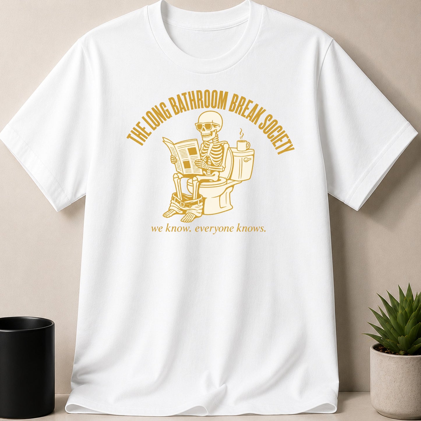 White t-shirt with graphic of skeleton on toilet reading newspaper and text.