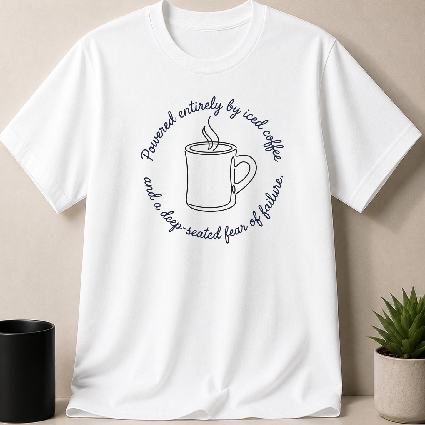 White t-shirt with circular text: "Powered entirely by iced coffee and a deep-seated fear of failure."