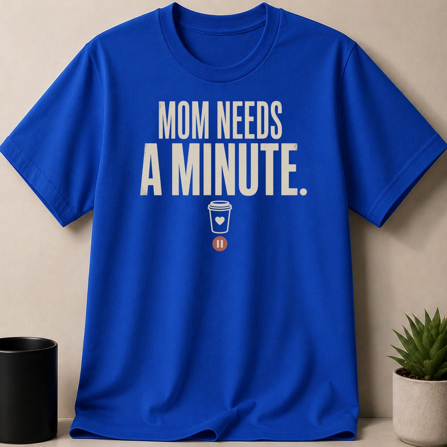 Blue t-shirt with "MOM NEEDS A MINUTE." text and a coffee cup icon.