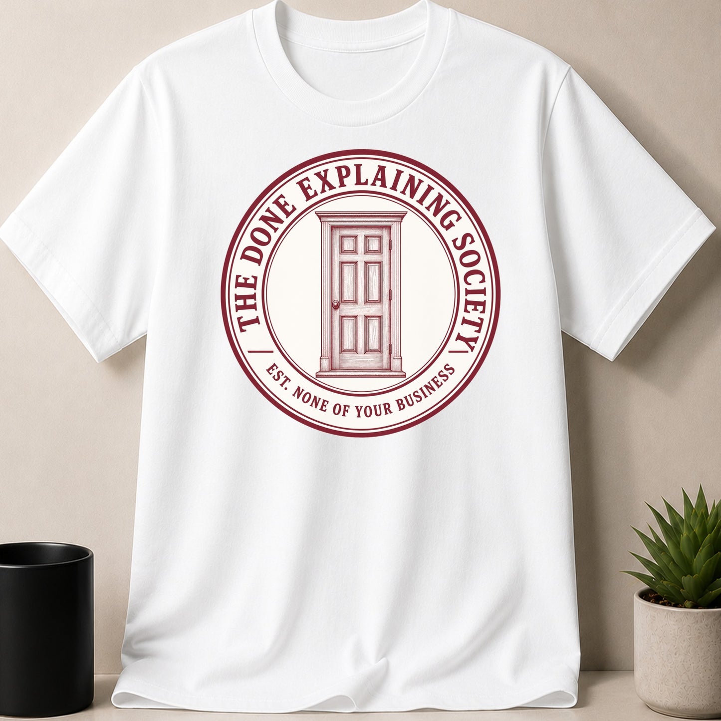 White t-shirt with maroon circular logo "The Done Explaining Society" and a door.