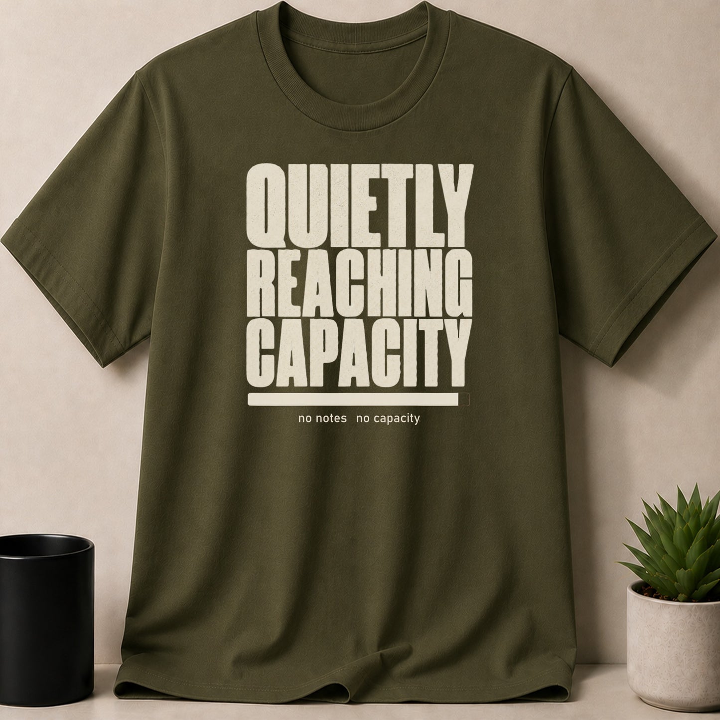 Olive t-shirt with white text "QUIETLY REACHING CAPACITY" and a progress bar.