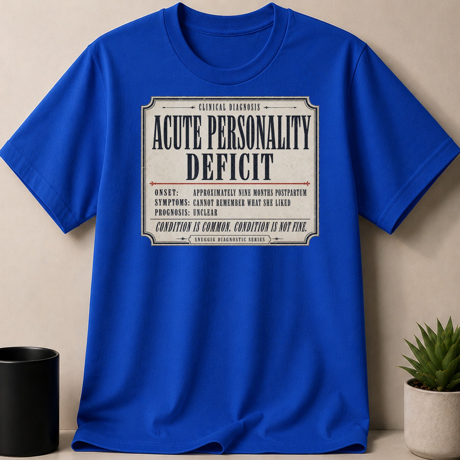 Blue t-shirt with "Acute Personality Deficit" clinical diagnosis text.