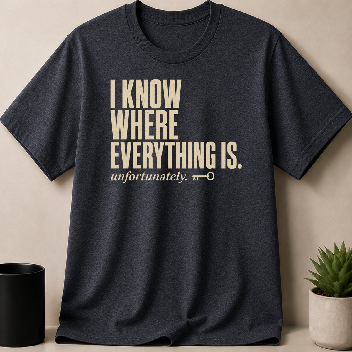 Dark grey t-shirt with text "I KNOW WHERE EVERYTHING IS. unfortunately." and a key icon.