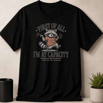 Black t-shirt with raccoon print: "First of all... I'm at capacity."